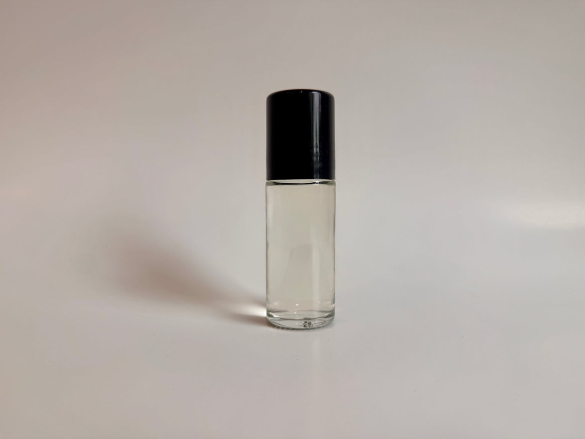 Clear glass roller bottle with black cap on a light gray background